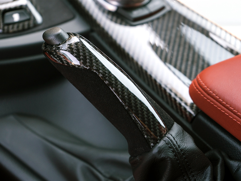 Close-up image of a Carbon Alcantara E-Brake Handle installed in a vehicle's interior, showcasing the black carbon fiber and Alcantara material.