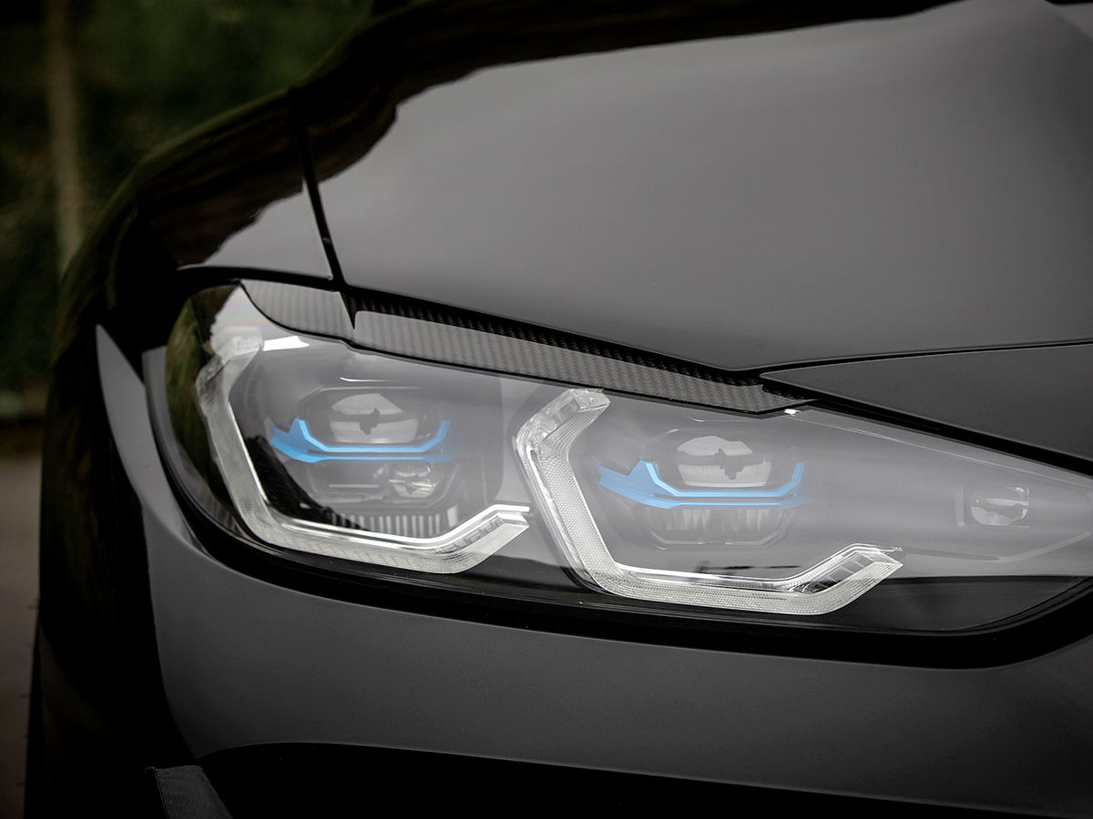 Close-up of carbon fiber headlight trim with a part of the vehicle's hood visible, showcasing the sleek design and texture of the trim.