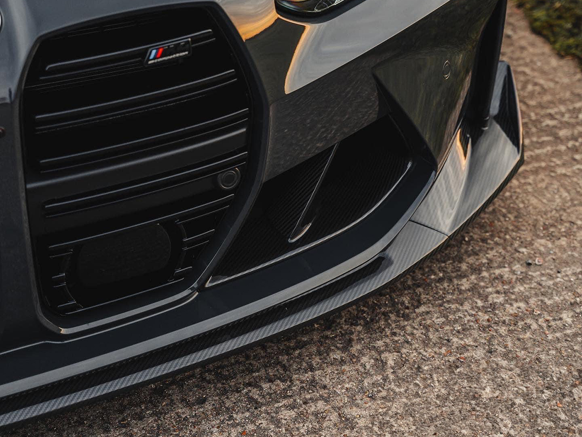 Close-up of a black carbon fiber front aero lip with a sleek finish attached to the front of a vehicle.