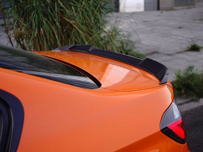 Close-up image of an orange car's trunk spoiler, which is black in color, showcasing the glossy carbon fiber finish.