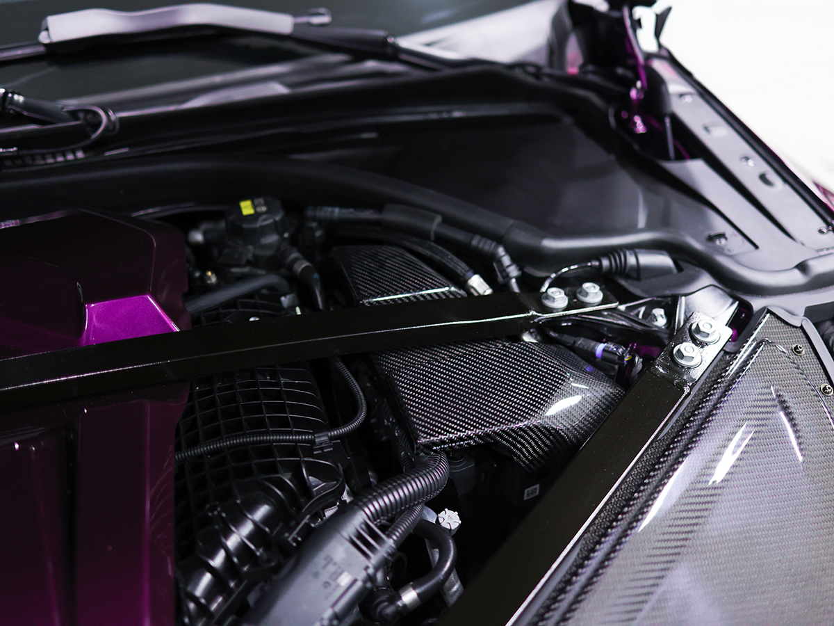 Close-up image of the AutoTecknic dry carbon ECU battery terminal cover installed on a vehicle, showcasing the carbon fiber texture and black finish.