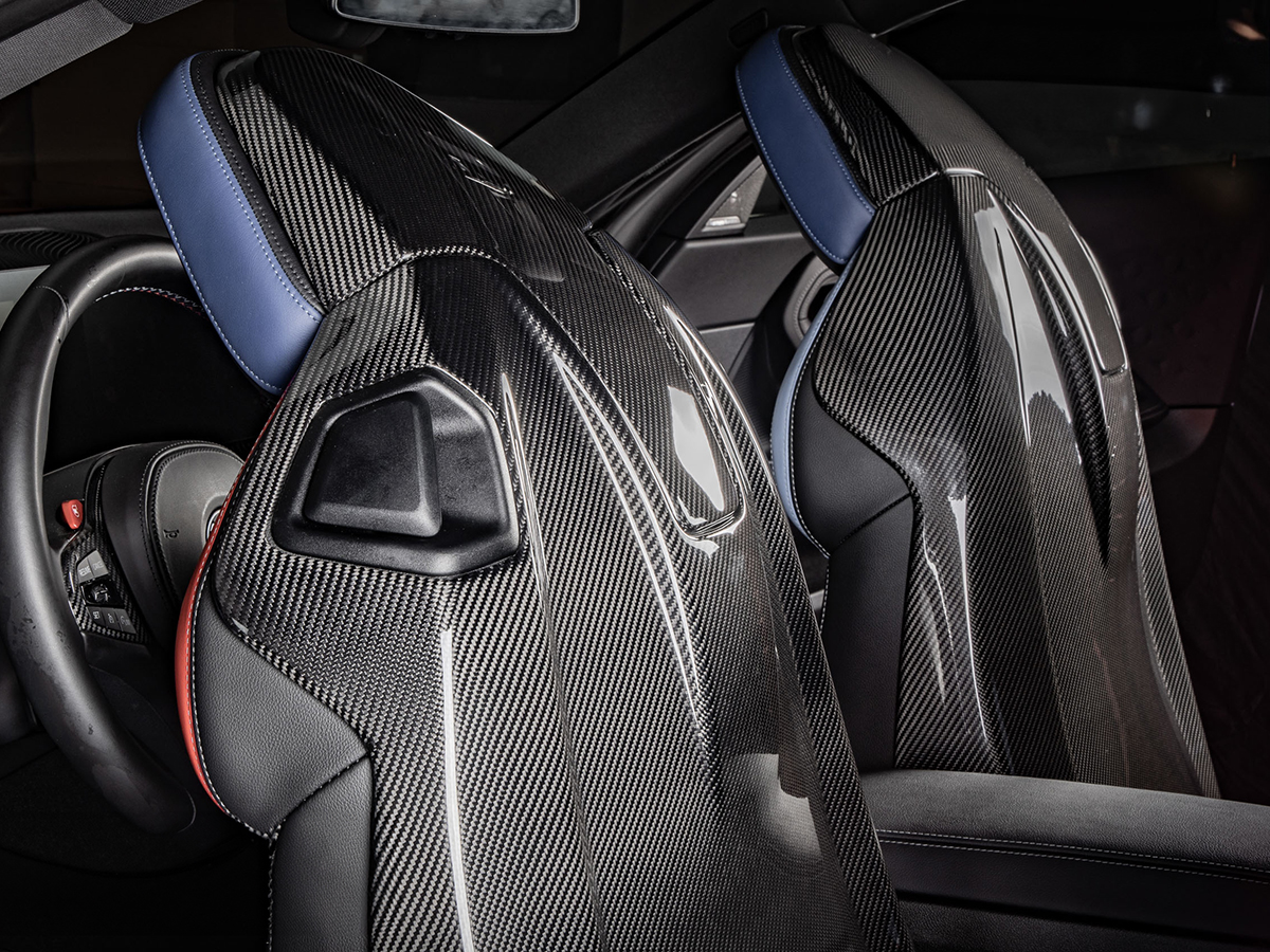A set of dry carbon full seat back covers installed in a vehicle's interior, featuring upper and lower portions for each seat with a glossy finish.