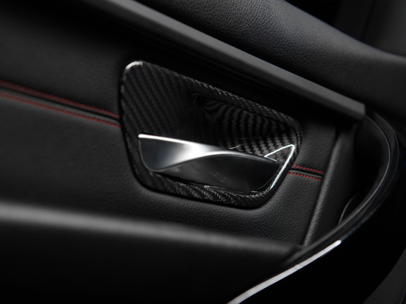 Close-up of a black and silver dry carbon interior door handle trim installed on a vehicle's door panel.