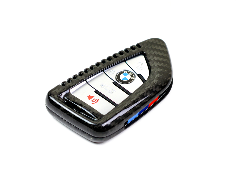 A black dry carbon fiber remote key case for a BMW, showcasing the high-gloss finish and the brand's logo.