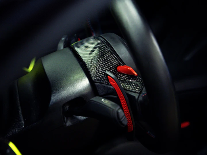 Close-up image of a black carbon fiber steering wheel top cover with a twill weave texture and red accents, designed for BMW M3 and M4 models.