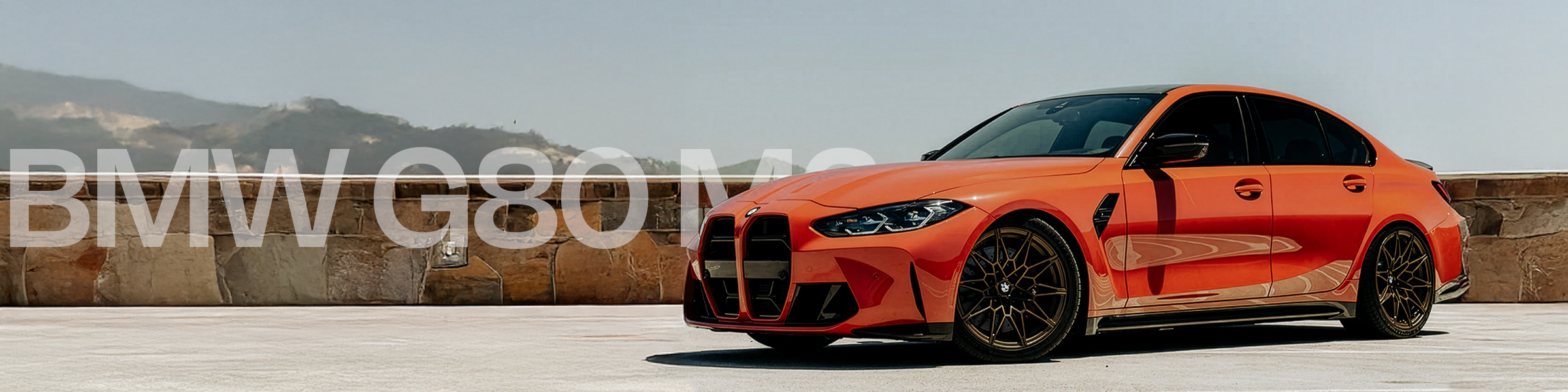 Orange BMW G80 M3 car on a road with mountains in the background
