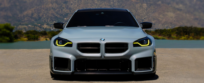 For the blog’s featured image of the M2, you could use:  **Alt text:** “Three-quarter front view of a BMW G87 M2 in metallic gray driving on an open road, highlighting its flared fenders and aerodynamic design”
