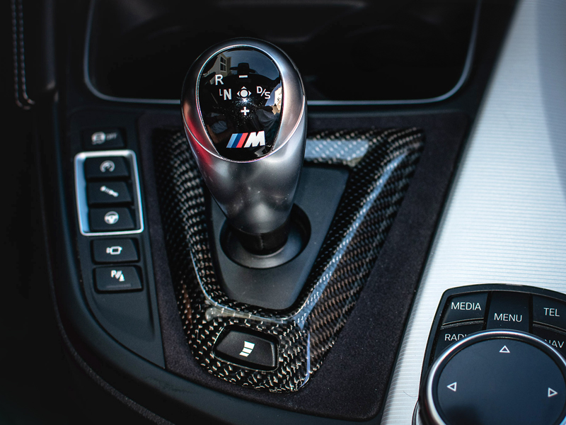 A carbon fiber and Alcantara shift console trim installed in the interior of a vehicle, featuring a shift knob with a BMW logo.
