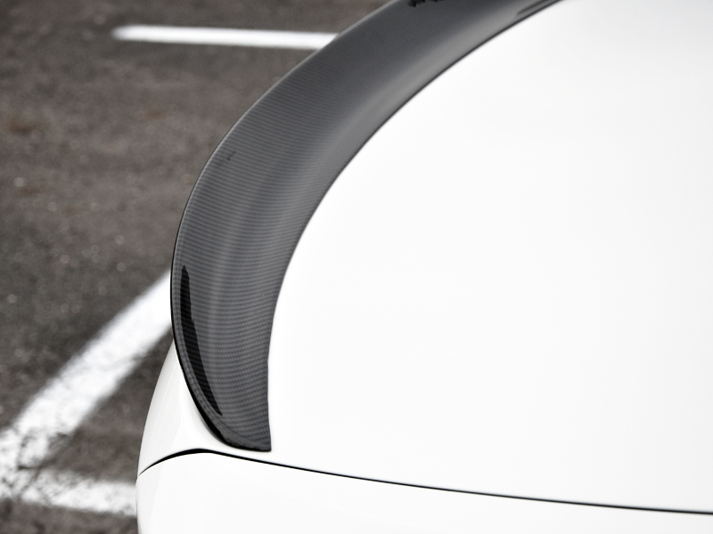 Close-up of a carbon fiber trunk spoiler for a car, attached to the rear of a vehicle.