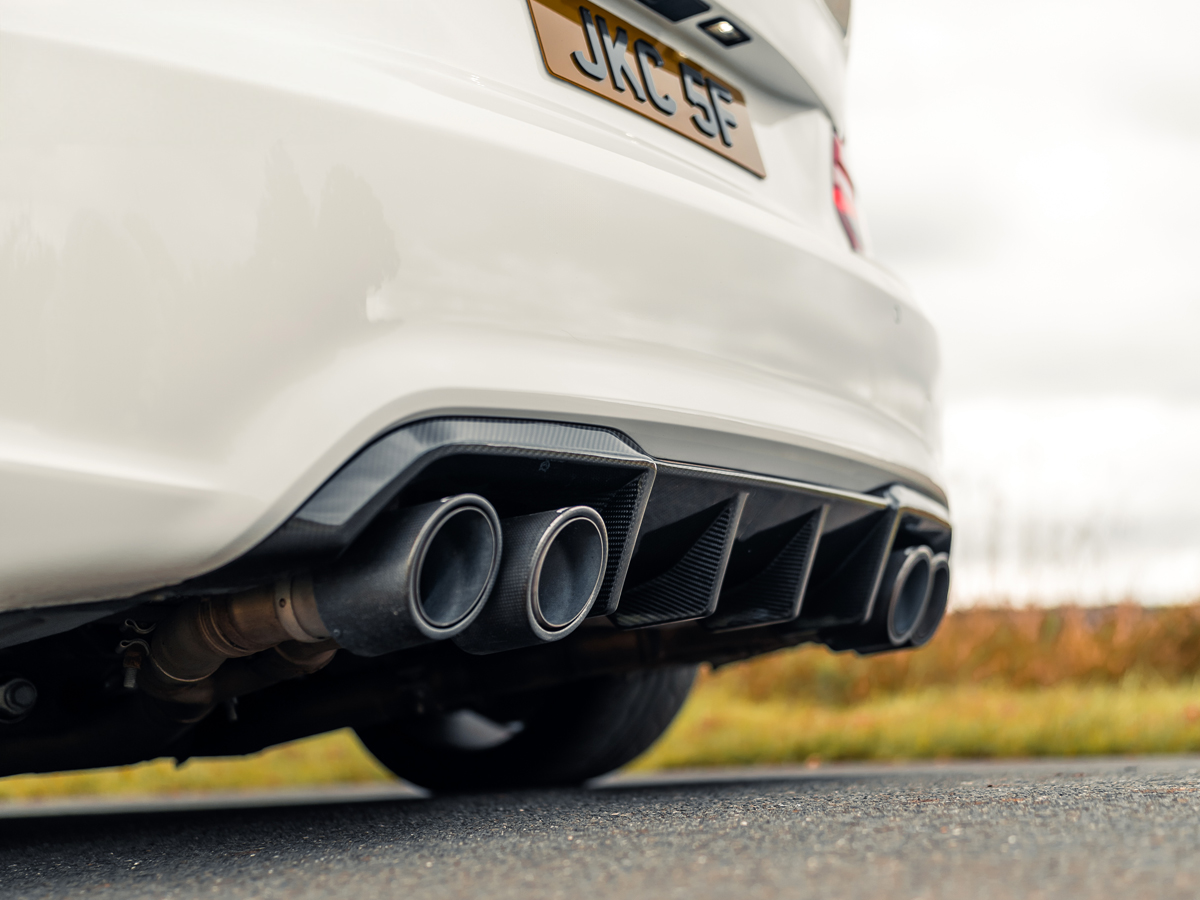 Rear diffuser of a white BMW vehicle featuring dual exhaust pipes and black carbon fiber material.