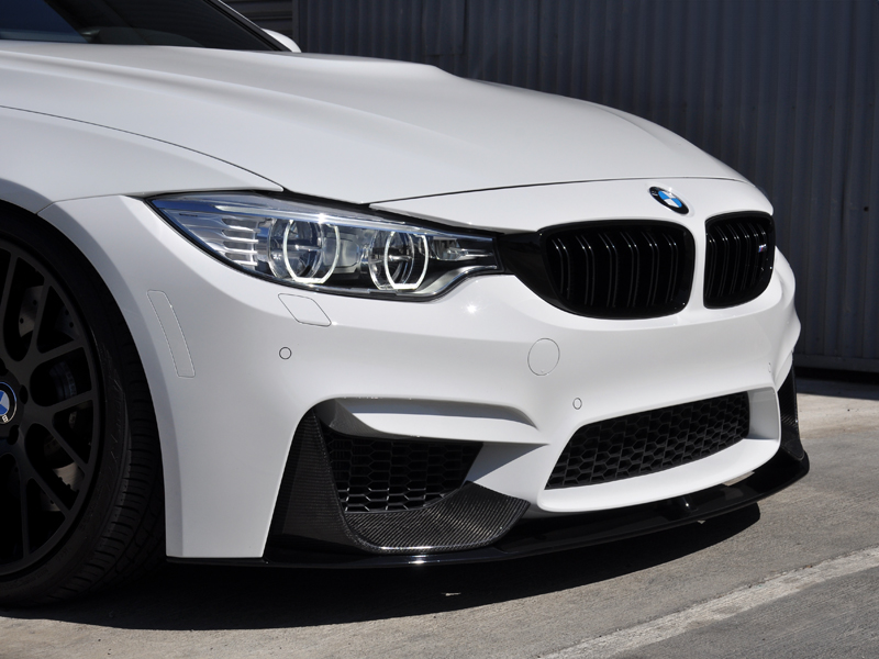 Front end of a white BMW with black carbon fiber aero splitters installed on the bumper.