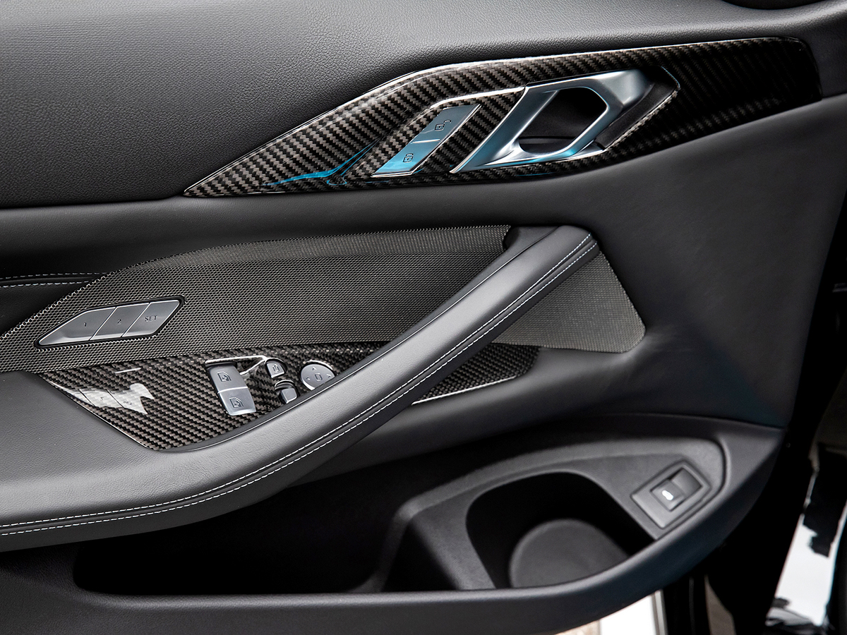 Close-up of black carbon fiber interior door handle trim installed on a vehicle's door panel.
