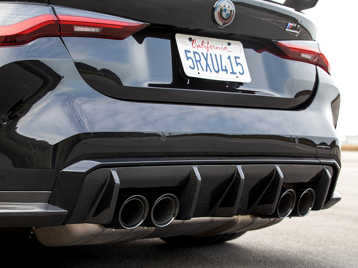 Rear diffuser of a car bumper made of dry carbon fiber, featuring multiple exhaust outlets and a black finish.