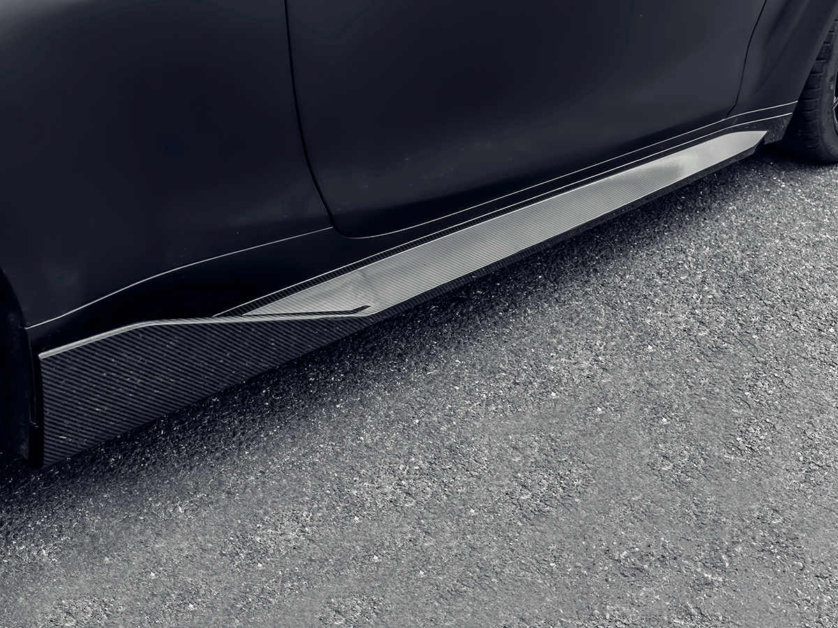 Close-up of a black car's side skirt made of carbon fiber.