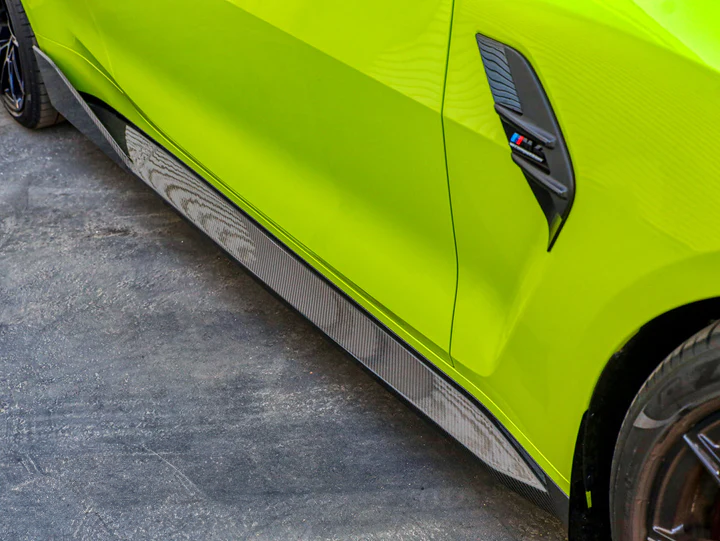 Close-up of a AutoTecknic dry carbon performante side skirt installed on a green vehicle, showcasing the texture and gloss finish.