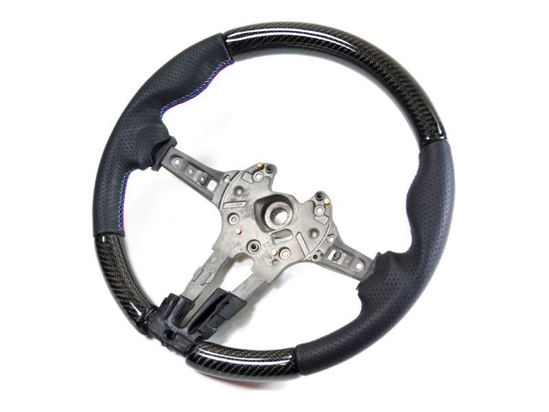 A carbon fiber steering wheel with black Alcantara suede grips and a twill weave carbon fiber finish.