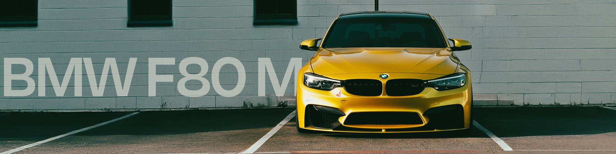 Yellow BMW F80 M car parked in front of a gray wall with 'BMW F80 M' text.