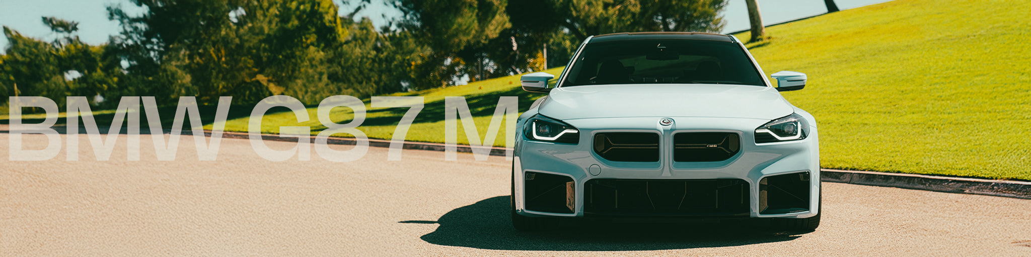 White BMW G87 M car on a road with greenery in the background