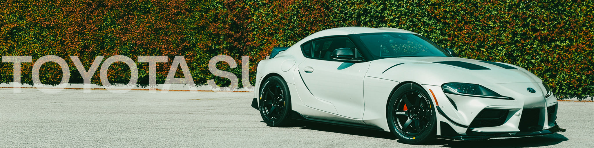 White Toyota Supra sports car on a road with 'Toyota' branding in the background.
